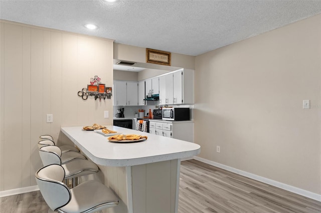 kitchen featuring black range with electric stovetop, light countertops, under cabinet range hood, light wood-style flooring, and a breakfast bar area