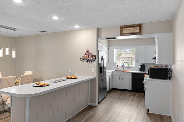 kitchen with light wood-style flooring, black appliances, a peninsula, and a textured ceiling
