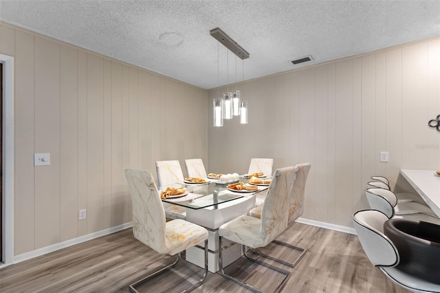 dining area featuring a textured ceiling, wood finished floors, baseboards, and visible vents