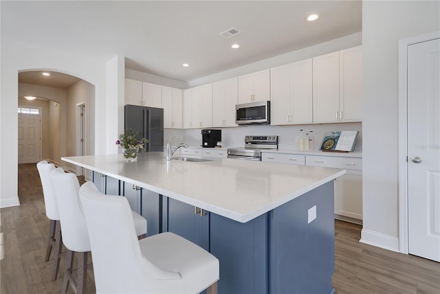 kitchen featuring stainless steel appliances, a sink, arched walkways, visible vents, and wood finished floors