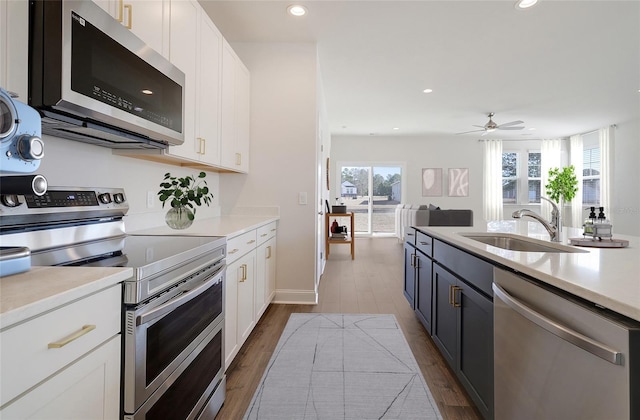 kitchen featuring stainless steel appliances, a sink, white cabinetry, a ceiling fan, and light countertops