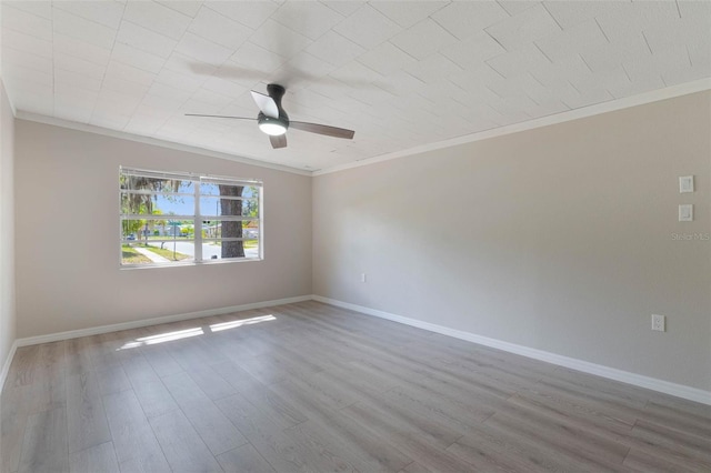 spare room with crown molding, wood finished floors, ceiling fan, and baseboards