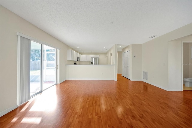 unfurnished living room with light wood-style floors, visible vents, and baseboards
