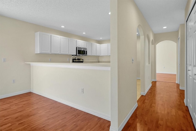 kitchen featuring light wood-style flooring, arched walkways, white cabinetry, stainless steel microwave, and baseboards