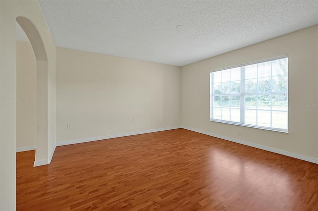 empty room featuring a textured ceiling, baseboards, and wood finished floors