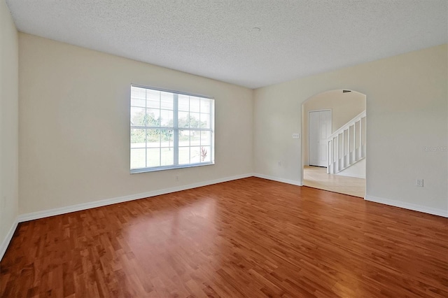 unfurnished room with arched walkways, wood finished floors, baseboards, and a textured ceiling