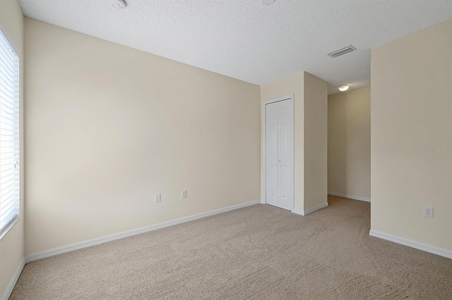 empty room featuring a textured ceiling, a healthy amount of sunlight, carpet, and visible vents