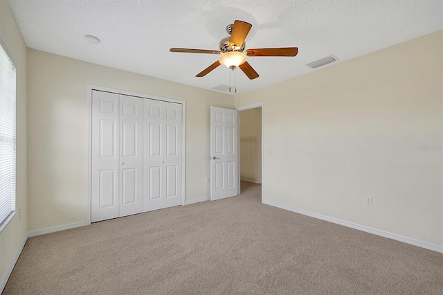 unfurnished bedroom with a textured ceiling, a closet, visible vents, carpet floors, and baseboards