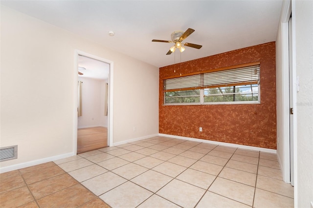 spare room featuring light tile patterned floors, visible vents, baseboards, and ceiling fan
