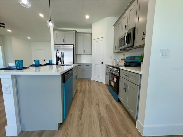 kitchen featuring stainless steel appliances, gray cabinetry, light wood finished floors, a kitchen island with sink, and light countertops