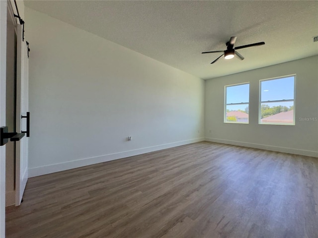 spare room featuring wood finished floors, ceiling fan, a barn door, baseboards, and a textured ceiling