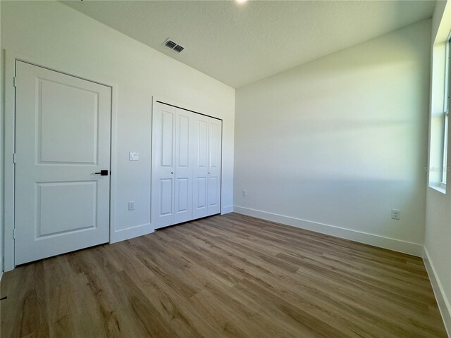unfurnished bedroom featuring baseboards, wood finished floors, a closet, and a textured ceiling