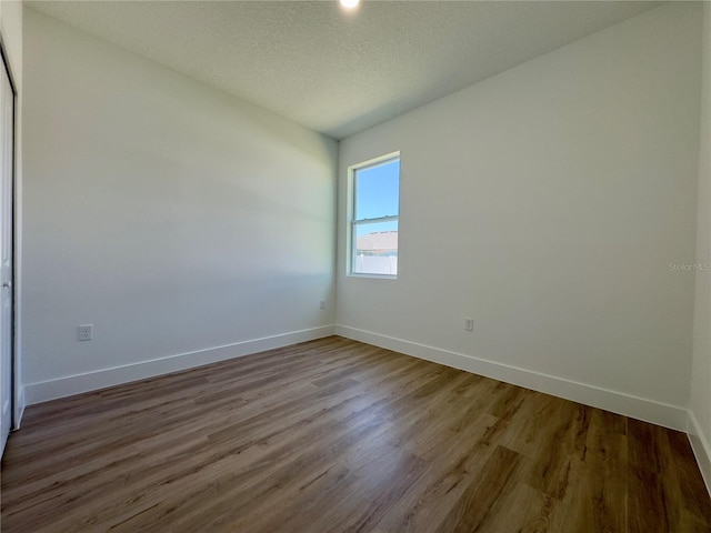 empty room with wood finished floors, baseboards, and a textured ceiling