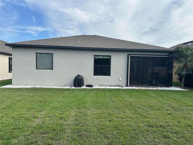 rear view of property with stucco siding, a sunroom, and a yard