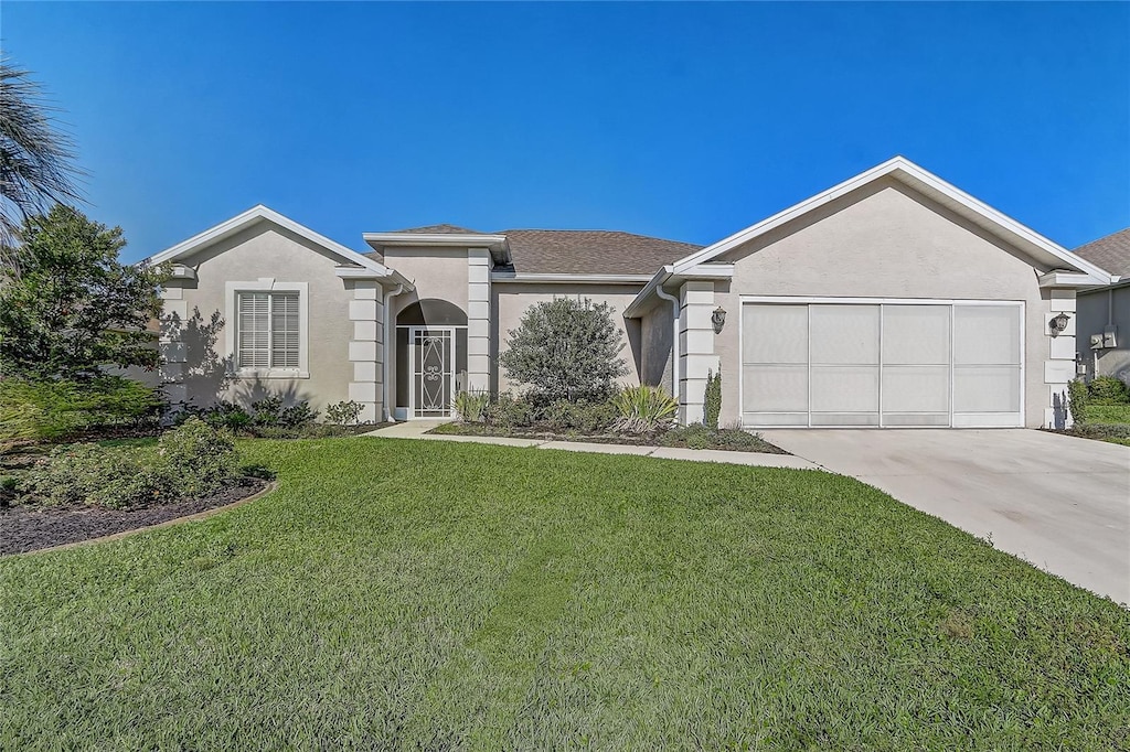 ranch-style home with concrete driveway, a front yard, an attached garage, and stucco siding