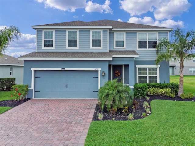 traditional-style house with a shingled roof, a garage, stucco siding, a front lawn, and decorative driveway