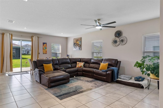 living room with a textured ceiling, light tile patterned floors, a ceiling fan, and visible vents