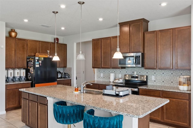 kitchen featuring light tile patterned flooring, a kitchen island with sink, a breakfast bar area, decorative backsplash, and appliances with stainless steel finishes
