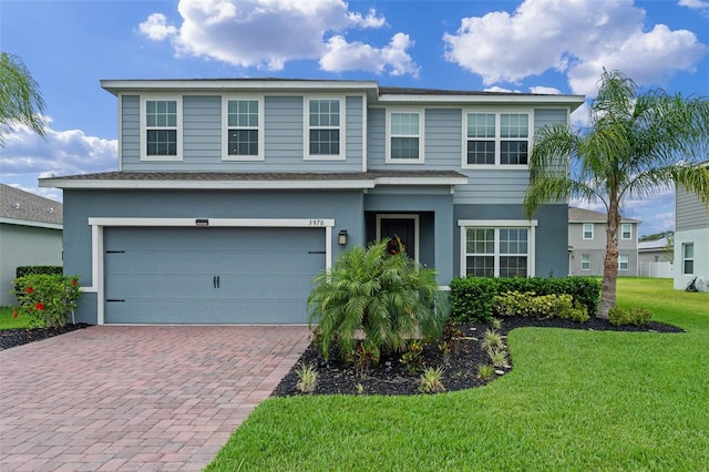 traditional home featuring a front yard, stucco siding, decorative driveway, and an attached garage