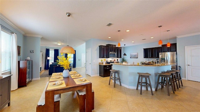 kitchen featuring appliances with stainless steel finishes, a kitchen bar, a large island with sink, pendant lighting, and light countertops