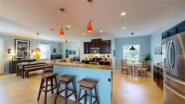 kitchen with appliances with stainless steel finishes, a breakfast bar area, an island with sink, stone countertops, and recessed lighting