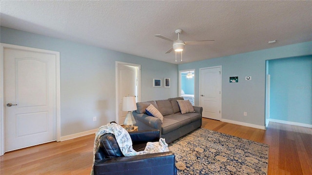 living area with ceiling fan, wood finished floors, baseboards, and a textured ceiling