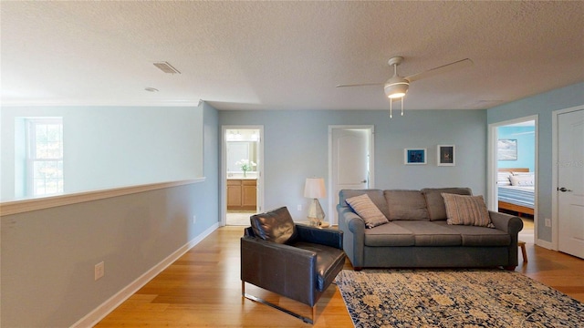 living room with light wood-type flooring, a textured ceiling, baseboards, and a ceiling fan