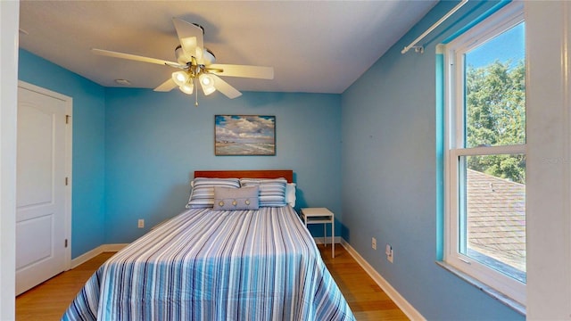 bedroom with multiple windows, wood finished floors, and baseboards