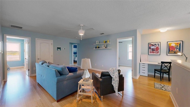 living room featuring light wood-style flooring, a textured ceiling, baseboards, and a ceiling fan