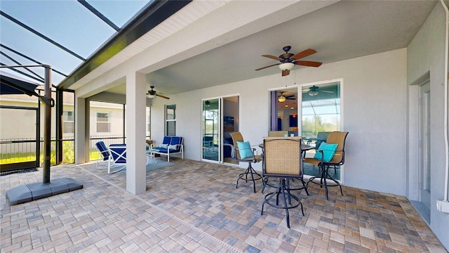 view of patio featuring ceiling fan, outdoor dining space, and glass enclosure