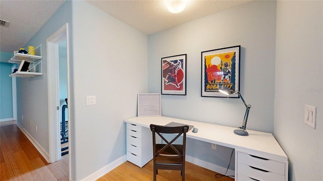 home office featuring light wood-style flooring, built in desk, baseboards, and a textured ceiling