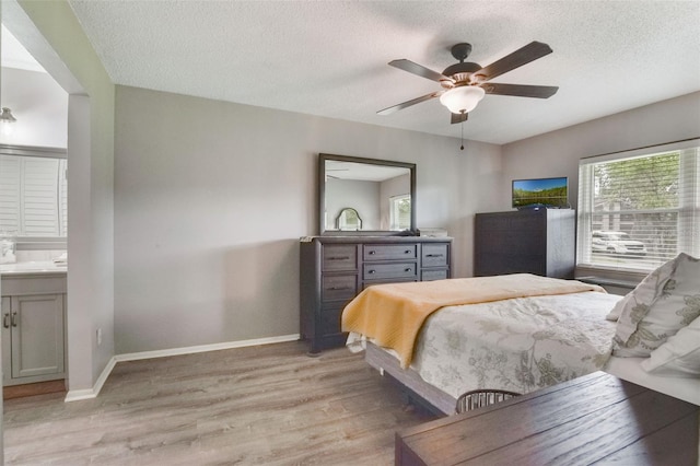 bedroom featuring ceiling fan, a textured ceiling, light wood-style flooring, baseboards, and ensuite bathroom
