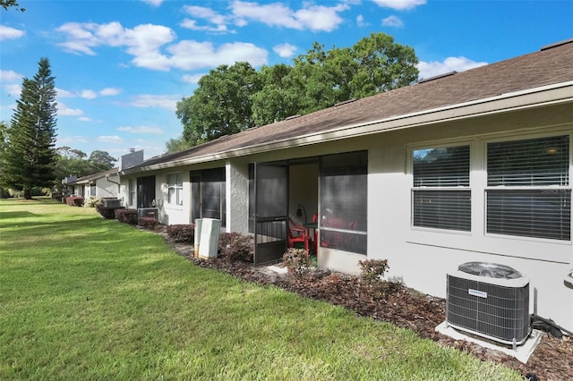 exterior space with roof with shingles, a sunroom, central AC unit, and a yard