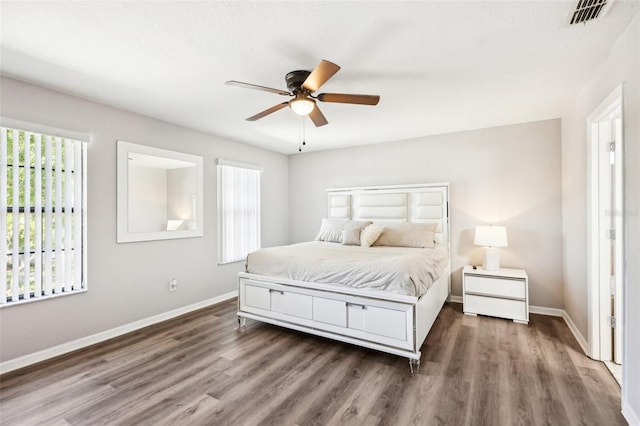 bedroom featuring ceiling fan, visible vents, baseboards, and wood finished floors