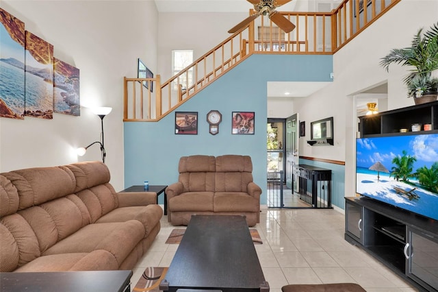 living room with a high ceiling, a ceiling fan, light tile patterned floors, baseboards, and stairs