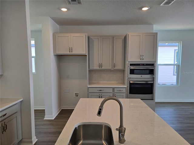 2980 Embark Trl, Saint Cloud, FL 34771 - kitchen featuring double oven, dark wood-style floors, gray cabinets, tasteful backsplash, and light stone counters
