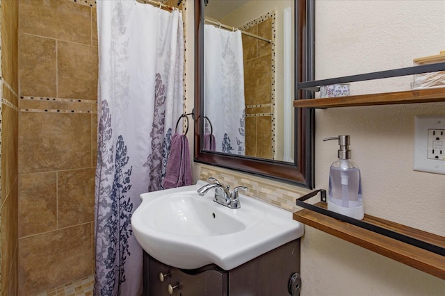 bathroom with a textured wall, tiled shower, vanity, and backsplash