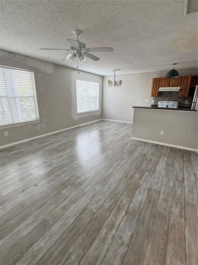 unfurnished living room with a textured ceiling, ceiling fan with notable chandelier, baseboards, wood finished floors, and visible vents