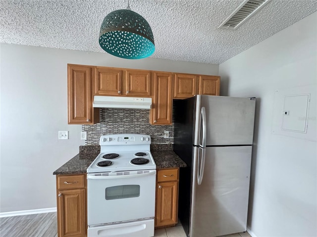 kitchen featuring visible vents, freestanding refrigerator, brown cabinetry, under cabinet range hood, and electric stove