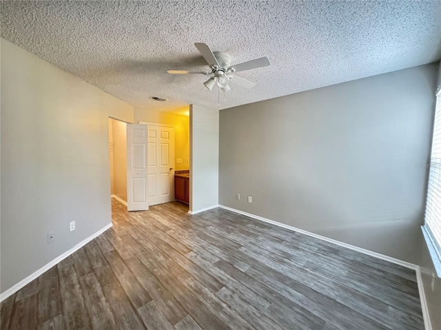 unfurnished bedroom featuring a ceiling fan, a textured ceiling, visible vents, dark wood finished floors, and baseboards
