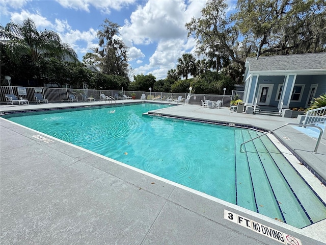 community pool with fence, an outdoor structure, and a patio area