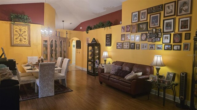living area featuring baseboards, vaulted ceiling, a chandelier, arched walkways, and wood finished floors