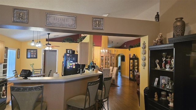 kitchen featuring a ceiling fan, freestanding refrigerator, dark wood-type flooring, a kitchen bar, and lofted ceiling