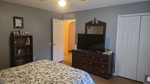 bedroom featuring visible vents, a closet, arched walkways, a ceiling fan, and wood finished floors