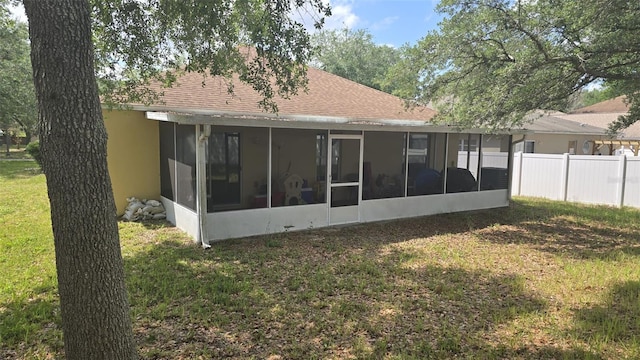 back of property featuring a sunroom, a yard, stucco siding, fence, and a shingled roof