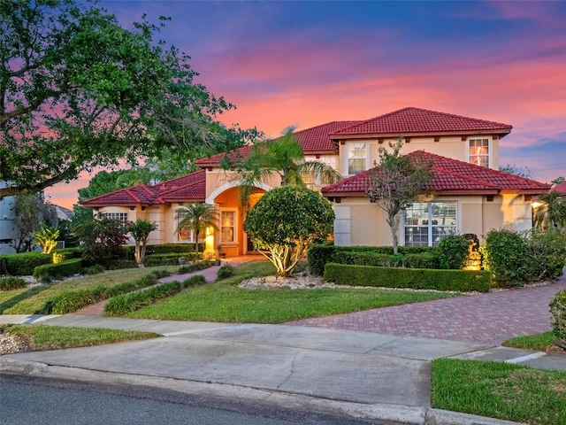 mediterranean / spanish home with a front yard, a tile roof, and stucco siding