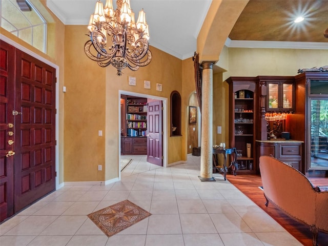 tiled entrance foyer with baseboards, an inviting chandelier, crown molding, ornate columns, and arched walkways