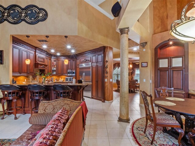 kitchen featuring decorative columns, light tile patterned floors, a peninsula, a towering ceiling, and stainless steel appliances