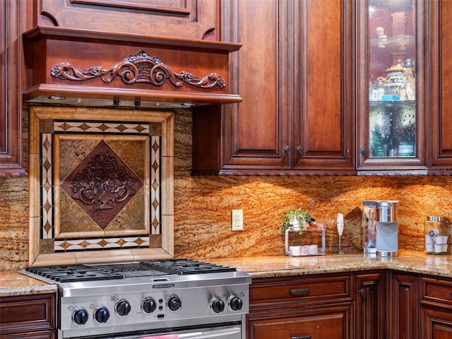 kitchen with tasteful backsplash, stove, light stone counters, and glass insert cabinets