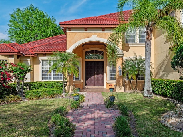 property entrance with stucco siding, a tile roof, and a lawn
